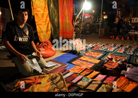 VIENTIANE, Laos - un fornitore visualizza i suoi tessuti per la vendita al mercato notturno sul Quai Fa Ngum sulle rive del Mekong in Vientiane, Laos. Foto Stock