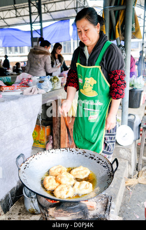 SAM NEUA, Laos - Una donna cuochi pasta fritta in un wok ampio del mercato mattutino in Sam Neua (anche ortografato Samneua, Xamneua e Xam Neua) nel nord-est del Laos. Foto Stock