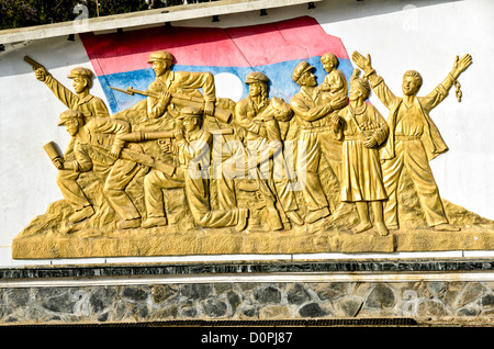 SAM NEUA, Laos - un grande fregio oro sull'indipendenza monumento nel centro cittadino di Sam Neua (anche ortografato Samneua, Xamneua e Xam Neua) nel nord-est del Laos. Esso raffigura il Lao lotta per l indipendenza, con soldati, gli agricoltori e i lavoratori in oro contro lo sfondo della bandiera Lao. Foto Stock