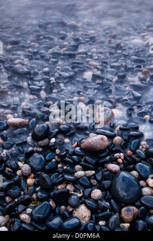 Wet, mare pietre levigate sulla riva della spiaggia Nanven, Cot Valley, Cornwall Foto Stock