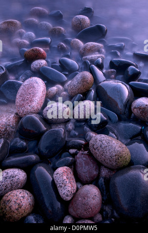 Wet, mare pietre levigate sulla riva della spiaggia Nanven, Cot Valley, Cornwall Foto Stock