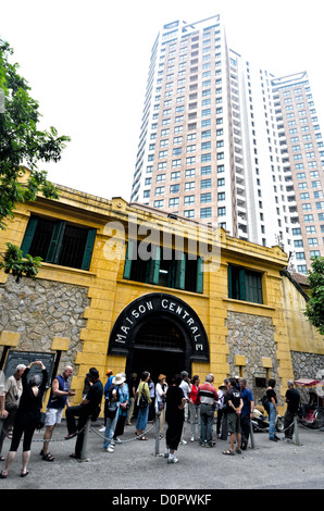 HANOI, Vietnam - in primo piano si trova l'ingresso principale della prigione di Hoa lo, con i turisti in piedi sul marciapiede. Sul retro c'è il nuovo edificio moderno che è stato costruito sulla maggior parte dello spazio precedentemente occupato dalla prigione. La prigione di Hoa lo, nota sarcasticamente come Hanoi Hilton durante la guerra del Vietnam, era originariamente una prigione coloniale francese per prigionieri politici e poi una prigione nordvietnamita per prigionieri di guerra. È particolarmente famosa per essere la prigione utilizzata per i piloti americani abbattuti durante la guerra del Vietnam. Foto Stock