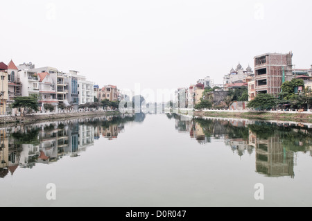 HANOI, Vietnam — Un canale nel Lago Ovest (ho Tay) ad Hanoi, Vietnam, con case e appartamenti su entrambe le sponde che si riflettono sulle acque calme. Foto Stock