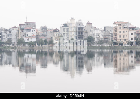 Edifici sulla riva si riflettono sulla superficie speculare del West Lake (Ho Tay) ad Hanoi, Vietnam, su un vago giorno. Foto Stock