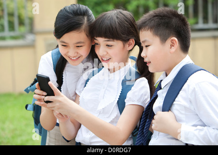 Gli scolari eccitati in uniforme con smart phone nel cortile della scuola Foto Stock