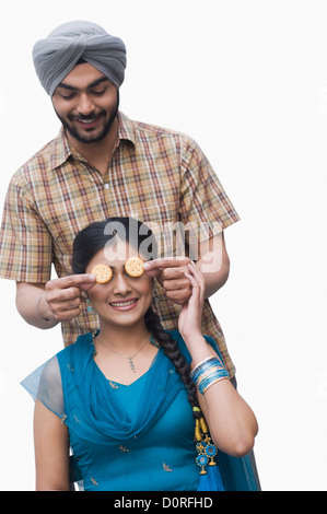 Uomo a copertura di sua moglie gli occhi con i cookie Foto Stock