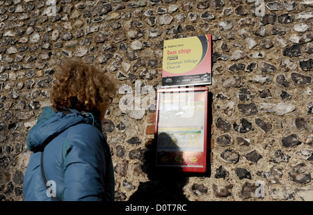 Donna controllo orari dei bus sul vecchio muro di pietra focaia nel villaggio rurale di impostazione Foto Stock