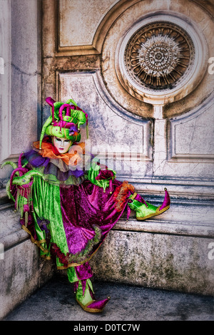 Partecipante mascherato vestito come un buffone durante il Carnevale di Venezia di fronte alla Basilica di Santa Maria della Salute Foto Stock