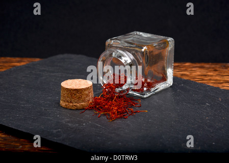 Lo zafferano spagnolo fuoriuscita da un vaso di vetro su di un naturale di ardesia. Foto Stock