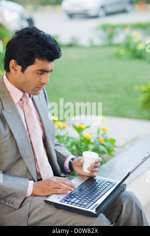Imprenditore lavora su un computer portatile in un parco, Gurgaon, Haryana, India Foto Stock