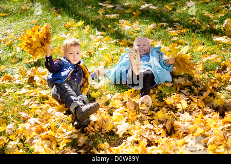 Angolo di alta vista di due giovani bambini giocosi in giallo le foglie di autunno che sono caduti sull'erba Foto Stock