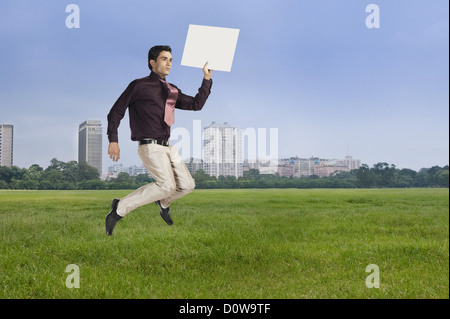 Businessman jumping con una targhetta vuota in un parco Foto Stock