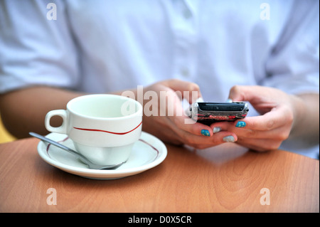 Uso gratuito della connessione internet wi-fi. Mani in possesso di un telefono cellulare e una tazza di caffè in un bar. Foto Stock