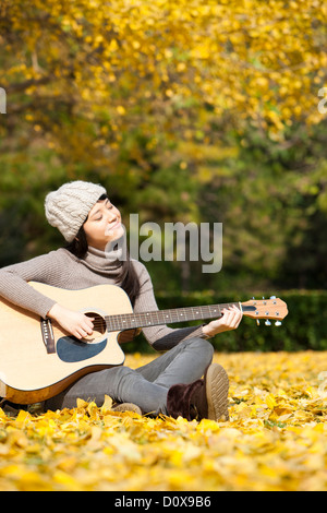 Bel collegio femminile studente di chitarra bagnata in autunno i raggi di sole del campus Foto Stock