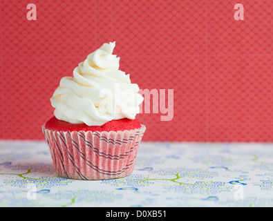 Tiny velvet cupcake con glassa bianca, sulla sommità di una carta decorata, isolato su sfondo rosso Foto Stock