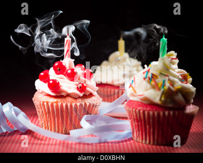 Tre differenti muffin con candele bruciato sul tavolo punteggiata rossa e sfondo nero fumo Foto Stock