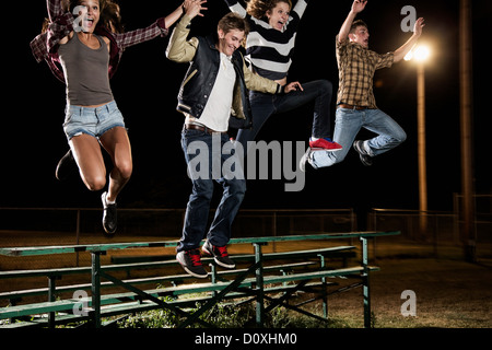 Quattro amici saltando su gradinate di notte Foto Stock