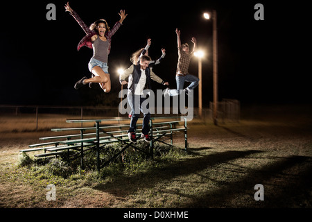 Quattro amici saltando su gradinate di notte Foto Stock