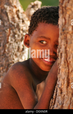 Africa i Boscimani della Namibia ritratto dietro tree bambino nascondendo clan di cacciatori-raccoglitori nomadi naturale primitiva sorridente Foto Stock