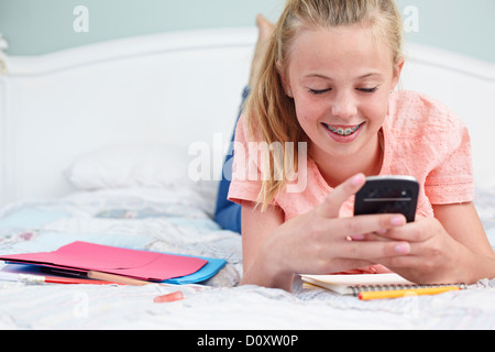 Ragazza adolescente sdraiato sul letto e tramite cellulare Foto Stock