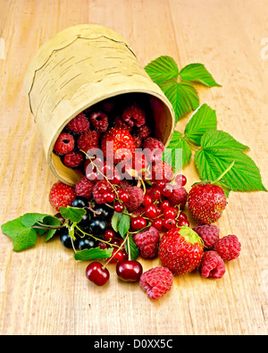 Ribes rosso e nero, lamponi, fragole, ciliegie con foglie verdi in una ciotola da corteccia di betulla su una tavola di legno Foto Stock