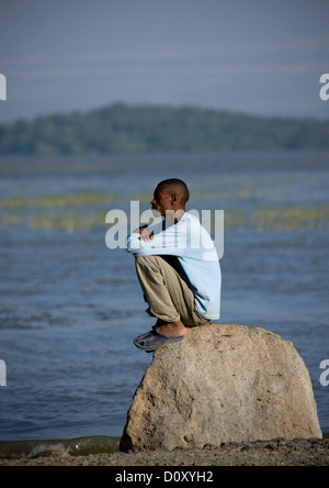 Oromo uomo seduto da solo su una roccia, Chamo Lake, Etiopia Foto Stock