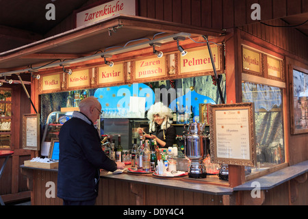 L'uomo l'acquisto di uno snack da una donna sorridente indossando una parrucca su un tradizionale mercatino di Natale in stallo di vendita di alimenti e bevande Alexanderplatz di Berlino, Germania Foto Stock