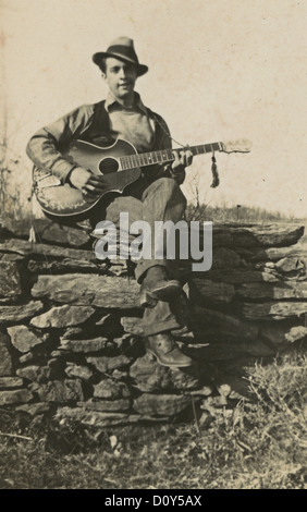 Circa 1910s fotografia, uomo di suonare una chitarra su un muro di pietra, probabilmente la Nuova Inghilterra, Stati Uniti d'America. Foto Stock
