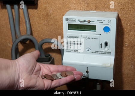 Titolare di pensione o di rendita nella povertà di combustibile mette una manciata di monete in un gas e misuratore di energia elettrica per mantenere in caldo in inverno Foto Stock