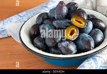 Prugne fresche (prugne) nel vaso su sfondo di legno, uno dimezzato Foto Stock