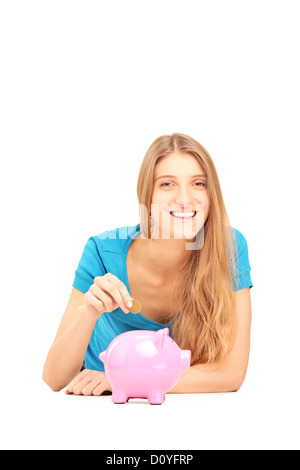 Donna sorridente mettendo una moneta in un salvadanaio isolata contro uno sfondo bianco Foto Stock