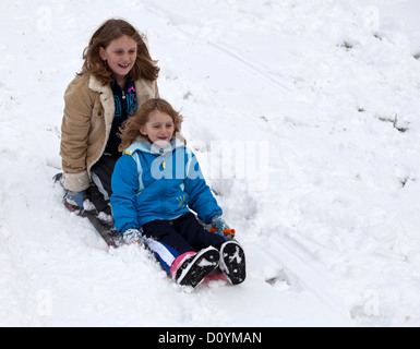 Due giovani ragazze lo scorrimento verso il basso di una collina in mezzo alla neve su una slitta. Foto Stock