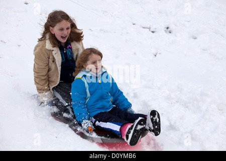 Due giovani ragazze lo scorrimento verso il basso di una collina in mezzo alla neve su una slitta. Foto Stock