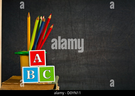 ABC e multicolori matita sul vecchio libro di testo contro la lavagna in classe. Il concetto di scuola Foto Stock