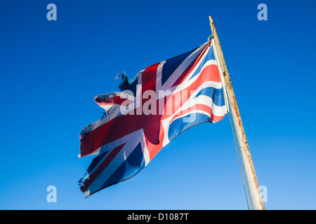 Ragged, lacerato e trascurato Union Jack, il British bandiera nazionale, su un palo di bandiera contro un cielo blu chiaro. Foto Stock