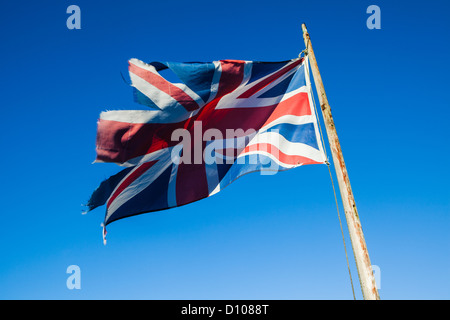 Ragged, lacerato e trascurato Union Jack, il British bandiera nazionale, su un palo di bandiera contro un cielo blu chiaro. Foto Stock