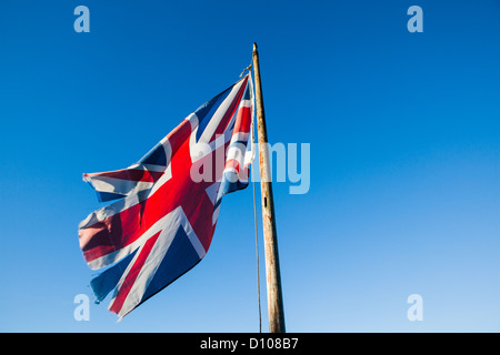 Ragged, lacerato e trascurato Union Jack, il British bandiera nazionale, su un palo di bandiera contro un cielo blu chiaro. Foto Stock