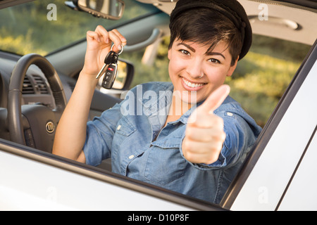 Sorridenti razza mista donna in auto con il pollice in alto tenendo premuto Set di chiavi. Foto Stock