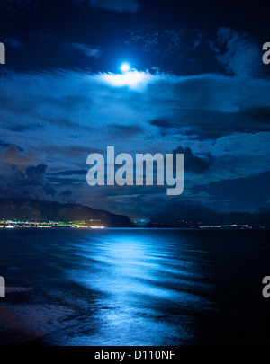 Città illuminata nella distanza accanto al mare di notte Foto Stock