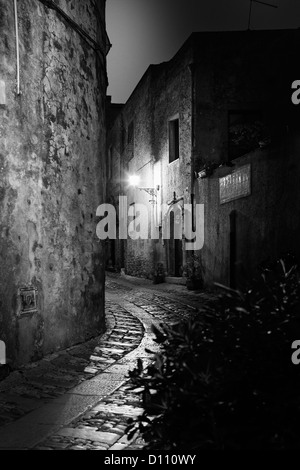 Curvato strada di ciottoli tra gli edifici in Sicilia illuminato da luci di strada Foto Stock