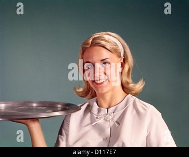 Anni sessanta DONNA BIONDA CAMERIERA HOLDING PORTAGIORNALI GUARDANDO sorridente della fotocamera Foto Stock