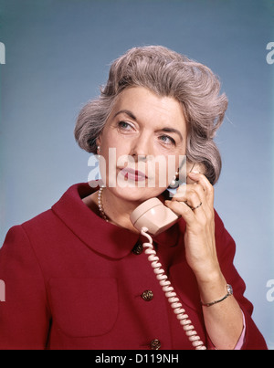 Anni sessanta senior di mezza età rosso donna Blusa espressione seria parlando al telefono Foto Stock