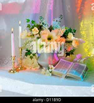 La Bibbia con bouquet di fiori bianchi per candele e multi luce colorata Foto Stock