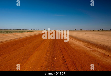 Rosso lungo outback australiano stradale attraverso il deserto arido paesaggio brulla e pianure del nord-occidentali del NSW Australia al lontano orizzonte Foto Stock