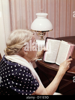 Anni sessanta donna anziana leggendo la Bibbia seduta a tavola Foto Stock