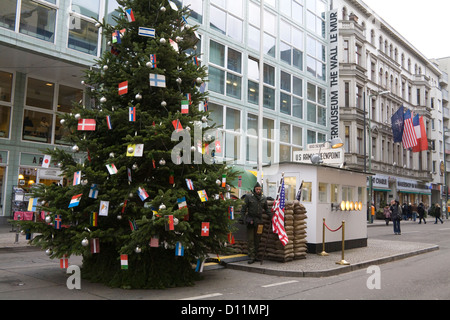 Berlino soldato americano tenendo a stelle e strisce di noi bandiera Checkpoint Charlie con museo del muro dietro e albero di Natale nella parte anteriore Foto Stock