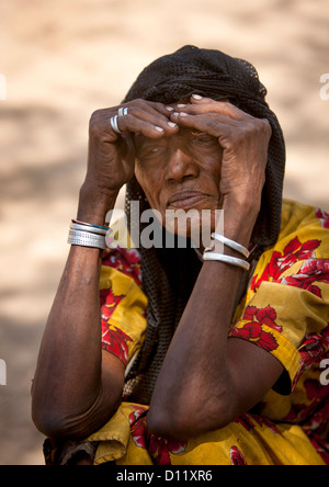 Ritratto di un vecchio Karrayyu tribù donna accovacciata e proteggere gli occhi dal sole, Metahara, Etiopia Foto Stock