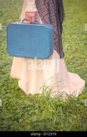 Una donna con un marrone scialle e una valigia blu Foto Stock