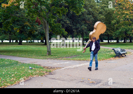 Un uomo che porta un contrabbasso attraverso Hyde Park di Londra, Inghilterra, Regno Unito Foto Stock