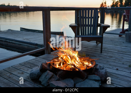 Una buca per il fuoco su una banchina in legno su un lago al tramonto; Lago di boschi Ontario Canada Foto Stock